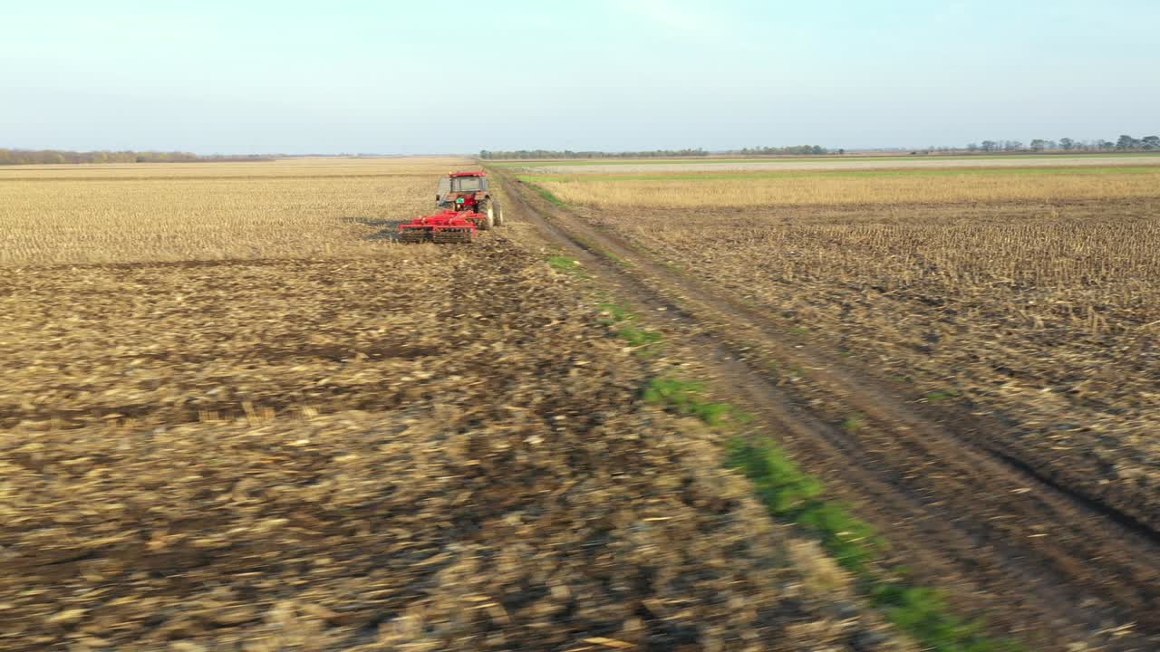vista lateral aérea de un tractor que arrastra una harra de disco sobre un campo agrícola, tierras de cultivo