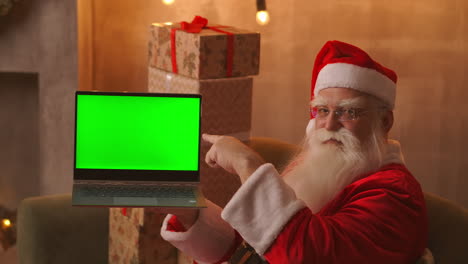 Santa-holds-a-laptop-with-a-green-screen-while-sitting-in-the-Christmas-decorations.-High-quality-4k-footage