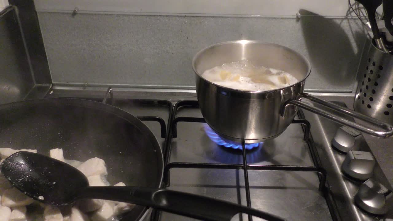 Pasta boiling in a pot and chicken meat frying in pan on stove top