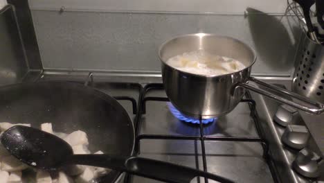 Pasta-boiling-in-a-pot-and-chicken-meat-frying-in-pan-on-stove-top