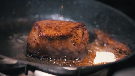 primer plano de un filete de carne frito en una sartén negra con mantequilla