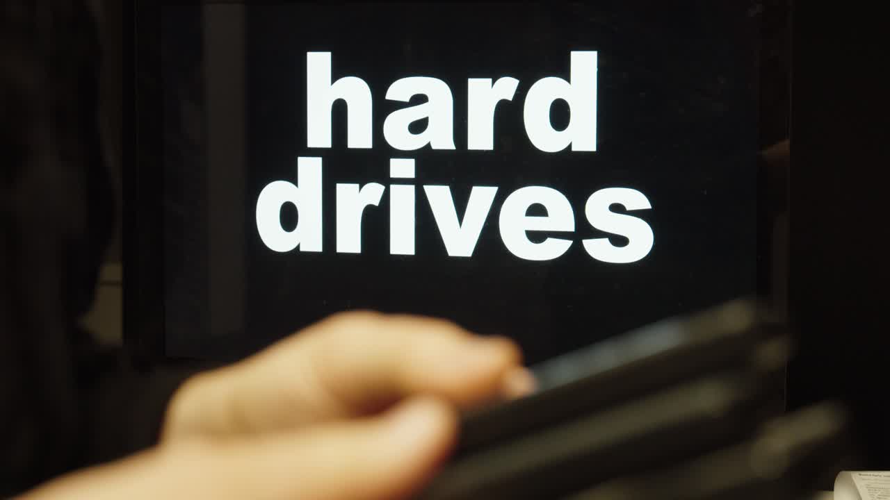 Close-up of a hand holding a hard drive in front of the words “hard drives,” representing data storage, backup solutions, and digital information technology