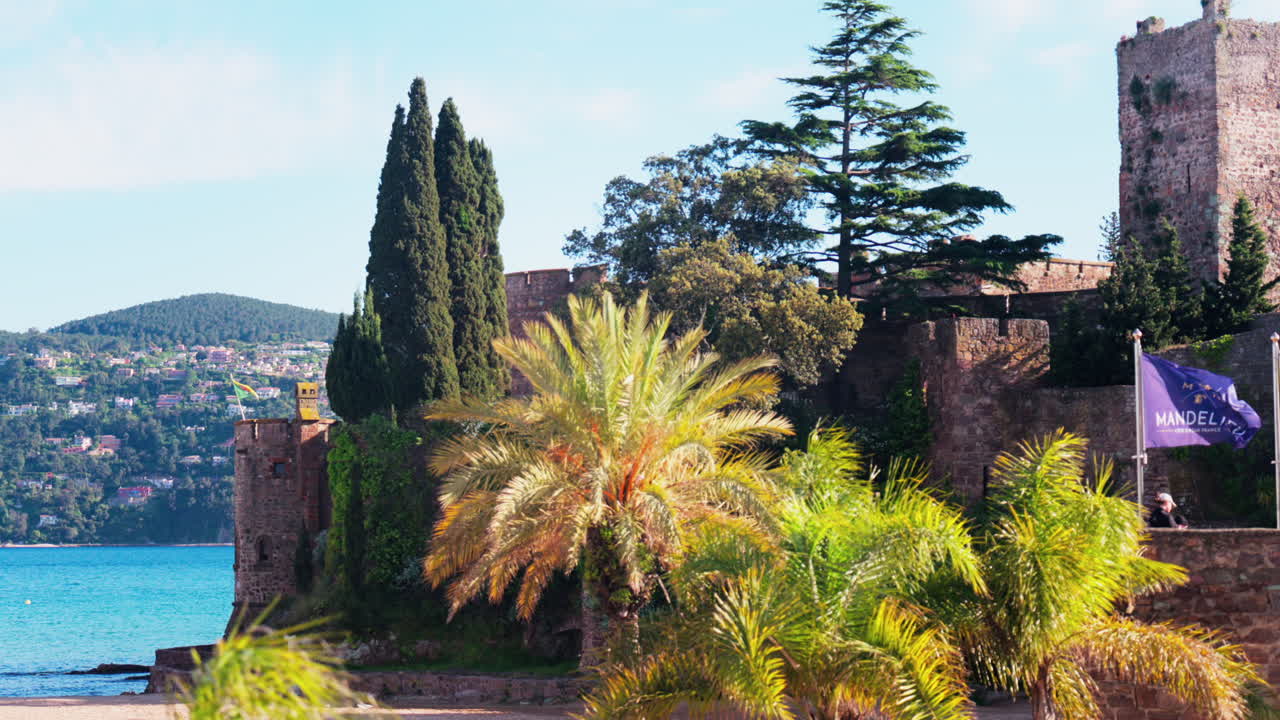 Mandelieu-La Napoule, France - May 10, 2025: View of two flags waving n front of the Chateau de la Napoule Castle on the shore of the Mediterranean Sea