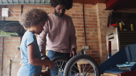 middle aged black father and his pre teen son standing at a workbench building a racing kart together in their garage