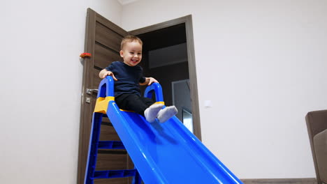 smiling baby boy climbing a plastic slide indoors. happy toddler playing cheerfully at home.