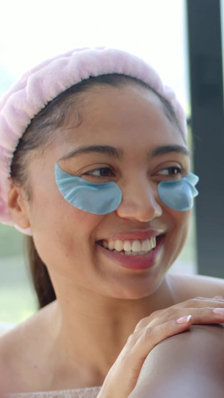 Vertical video: Talking woman in headband showing blue eye patches, resting on friend's arm at home