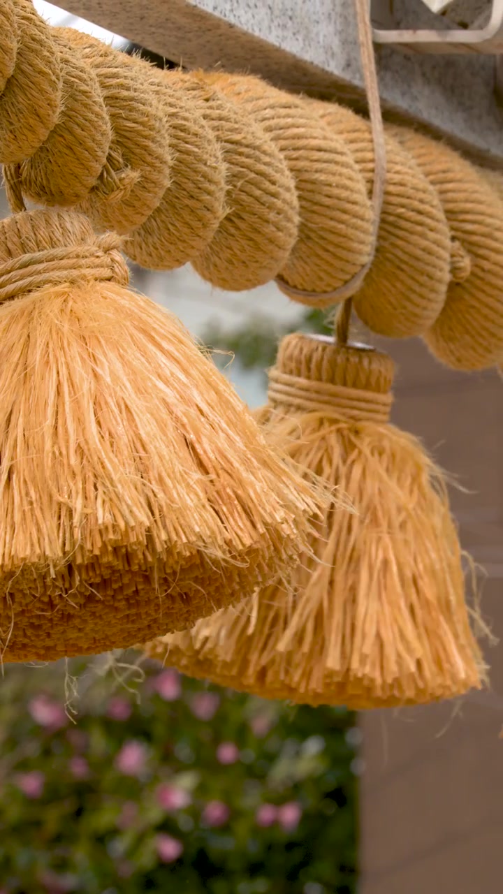 Primo piano di una spessa corda shimenawa di paglia e nappe appese a un cancello di pietra.