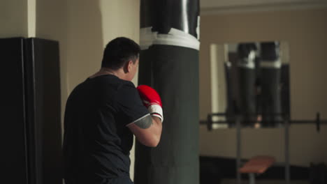 sportsperson punches hanging bag training in sports club. athlete exercises boxing technique with inventory in fighting gym slow motion. combat attack