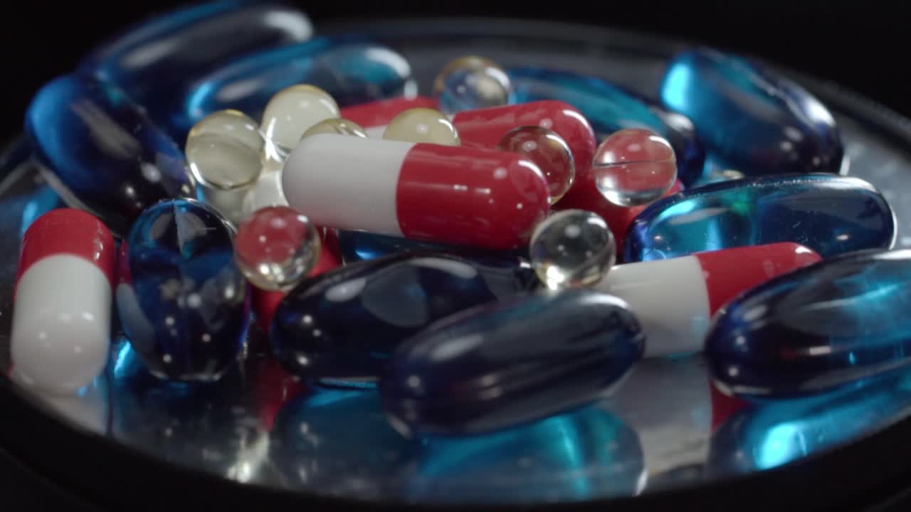 Close up shot of red, white and blue capsules rotating together with transparent softgel pills