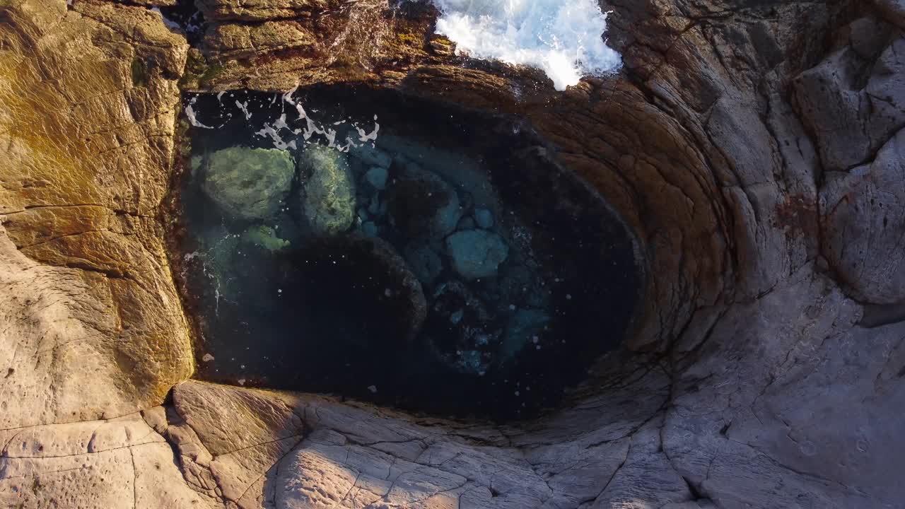 Amazing top down aerial shot of natural circular pool, waves crashing inside
