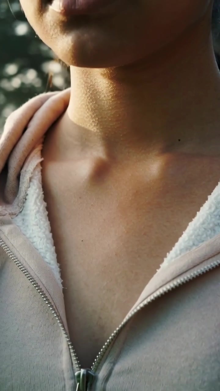 Video verticale: Una donna che alza entrambe le mani, sistemando i lacci della felpa con cappuccio all'aperto vicino agli alberi.