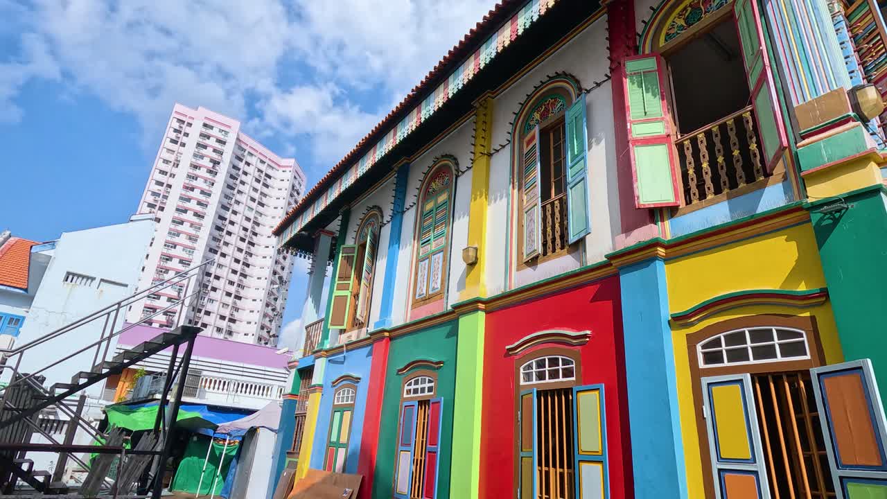Vividly painted shophouse with ornate windows and doors, captured in bright daylight with upward camera movement, highlighting architectural details and vibrant colors