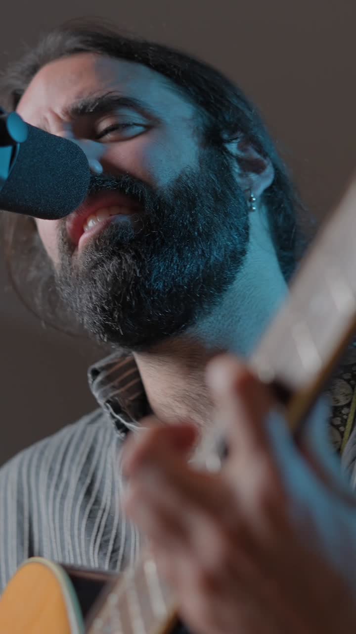A man with a beard singing and playing guitar into a microphone