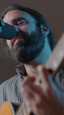 a man with a beard singing and playing guitar into a microphone