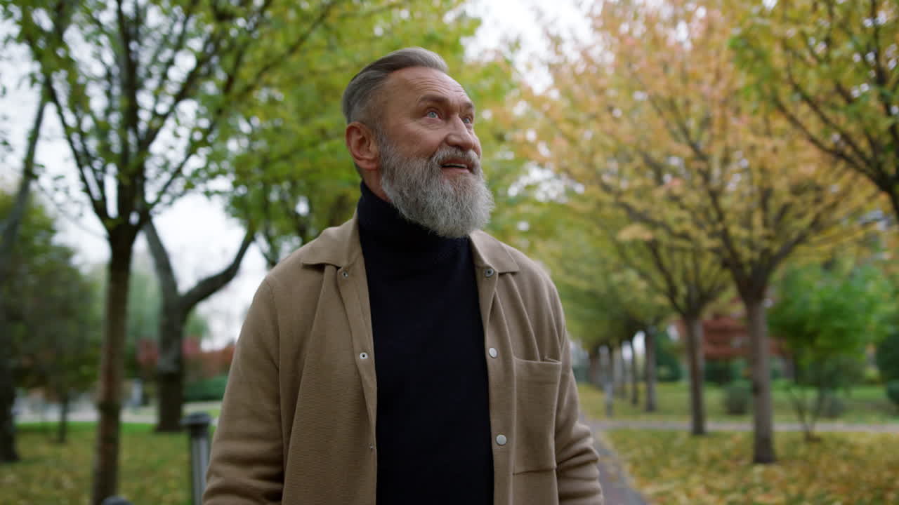 retrato de un hombre maduro y atractivo con una sonrisa feliz mirando alrededor del parque de otoño.
