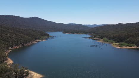 Slow-Moving-drone-shot-of-Sunny-Blue-water-and-Green-Trees-and-Mountains,-Near-Lake-Eildon