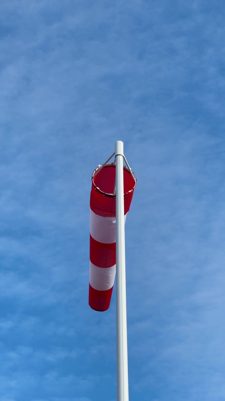 Red and White Windsock Blowing in Strong Wind Against Sky