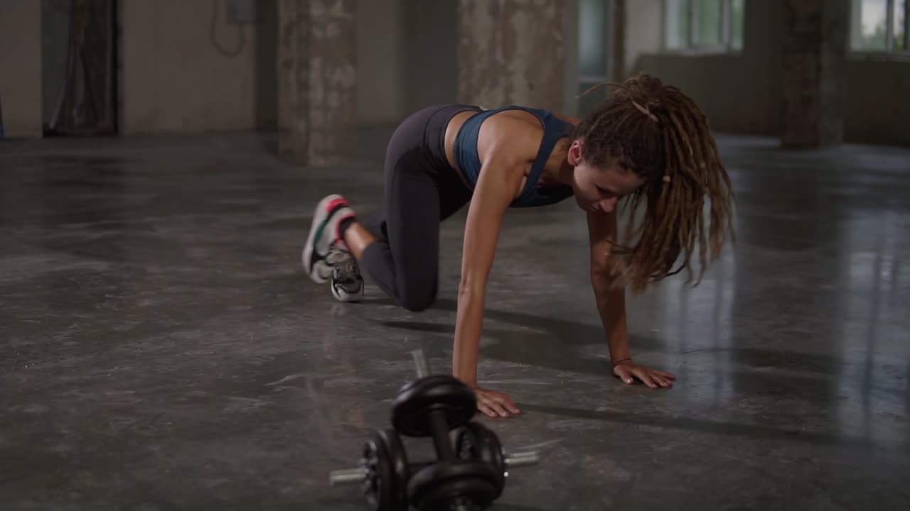 Young sporty stylish woman train her body workout her muscles indoor at empty studio. Athletic beautiful styylish woman with long dreadlocks does running plank exercise