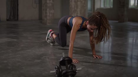Young-sporty-stylish-woman-train-her-body-workout-her-muscles-indoor-at-empty-studio.-Athletic-beautiful-styylish-woman-with-long-dreadlocks-does-running-plank-exercise
