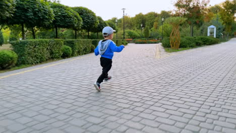 year and half toddler boy running happily by the paved path. following the kid running by the beautiful park.