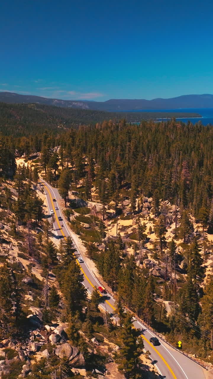 Rising over the mountainous landscape covered with pine tree forest. Road through the wood in the rocks. Blue lake at the foot of mountains. Vertical video