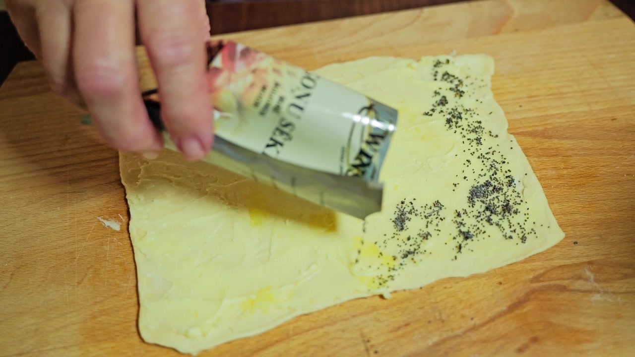 Poppy seeds are sprinkled evenly over puff pastry before shaping homemade rolls