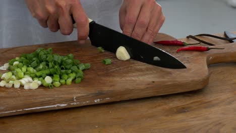 slicing a glove of garlic among celery and chillies on a cutting board