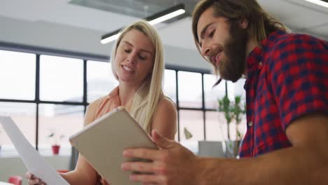 Caucasian-business-people-using-digital-tablet-going-through-paperwork-in-modern-office