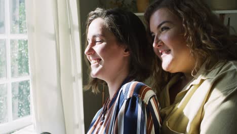 caucasian lesbian couple embracing and looking through window