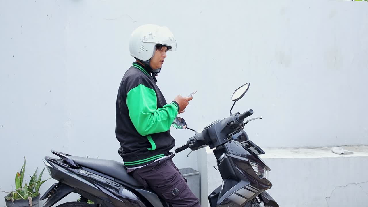 Motorcycle taxi driver using smartphone while waiting for next fare on motorcycle taxi vehicle