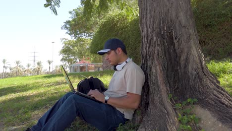 man with cap using laptop in park. the scene is peaceful and relaxing, enjoying his time outdoors.