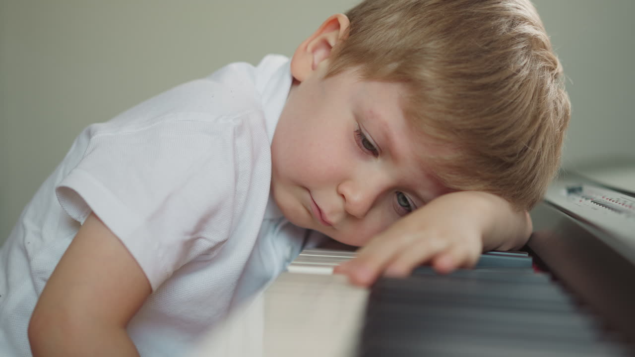 아이 는 졸음 을 느끼고 피아노 에 머리 를  ⁇ 고 앉는다