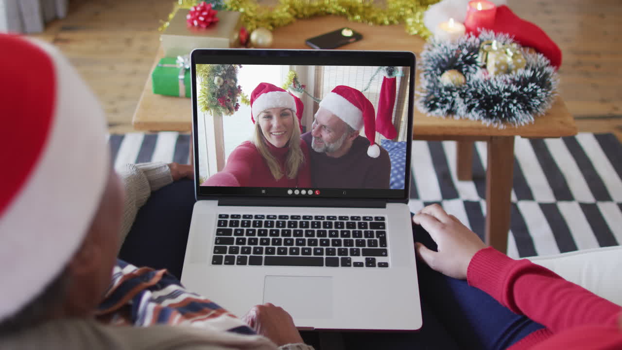 madre y hija afroamericanas usando una computadora portátil para una videollamada de navidad con la pareja en la pantalla