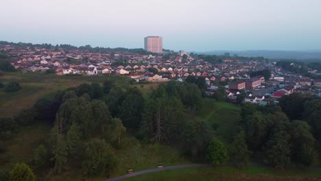 retreating aerial shot of large giant office building surrounded by residential houses at sunrise with green trees and fields in park nearby