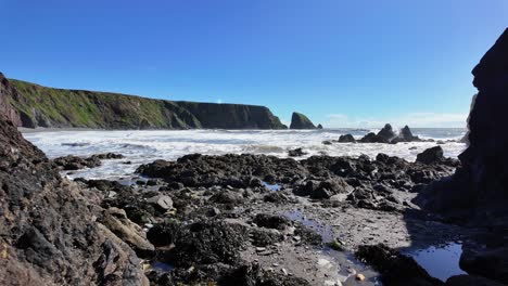 Surf-Rompiendo-En-Una-Playa-Rocosa-Con-Acantilados-Y-Pilas-De-Mar-En-La-Costa-De-Cobre-De-Ballydwane,-Waterford,-Irlanda,-En-Un-Perfecto-Día-De-Primavera