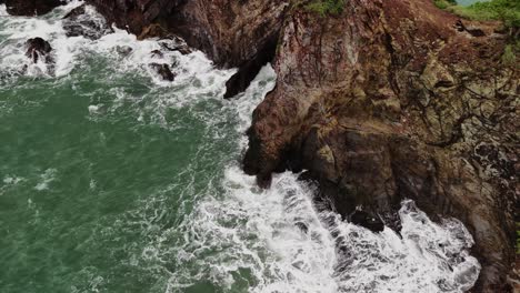 aerial shot of waves crashing against island rocks