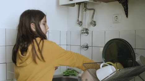 chica de pie y lavando los platos en la cocina.