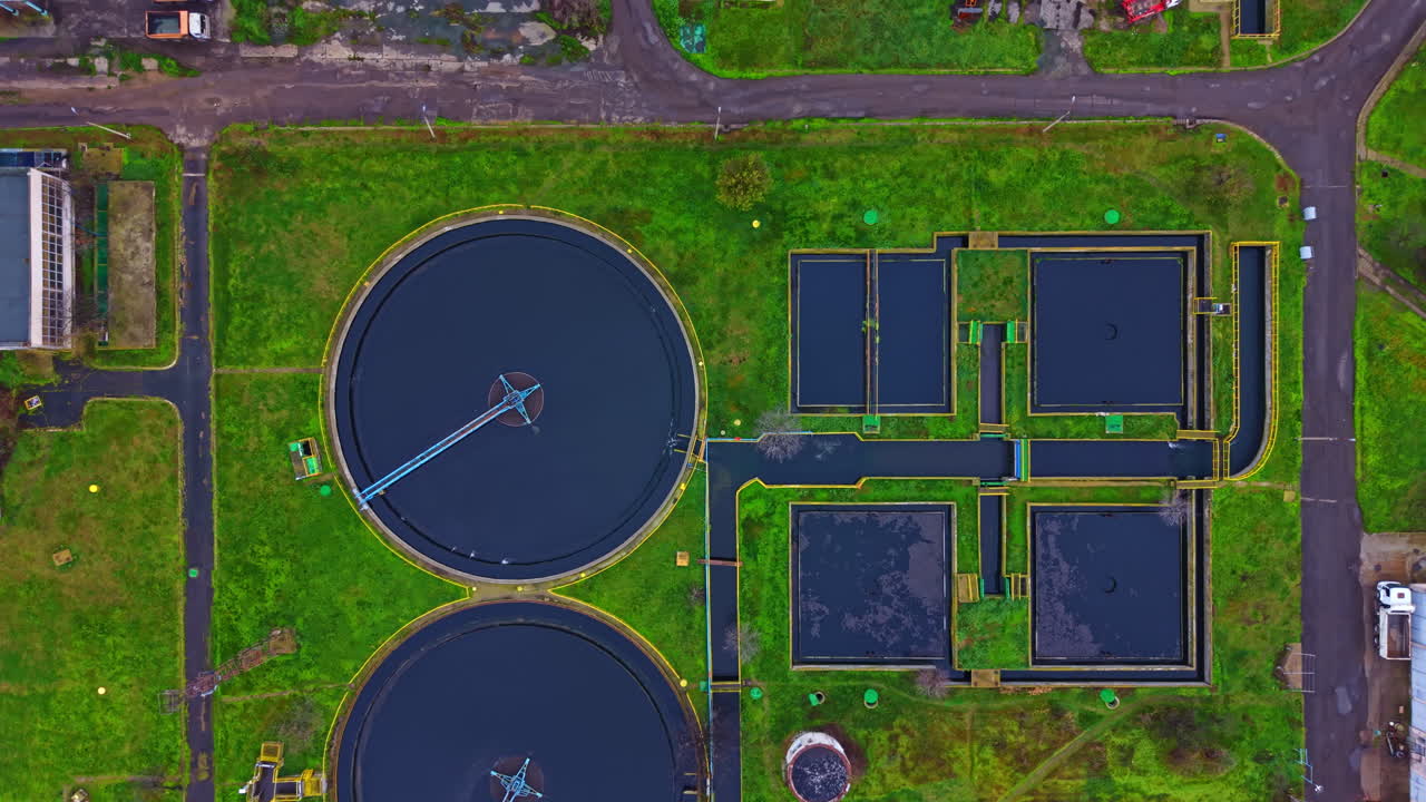 Large water treatment facility with circular tanks and green landscape in daytime over urban area