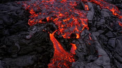 the footage from a 4k drone reveals a thick stream of lava moving slowly and cascading, resembling a crawling motion as it advances across dried lava rocks