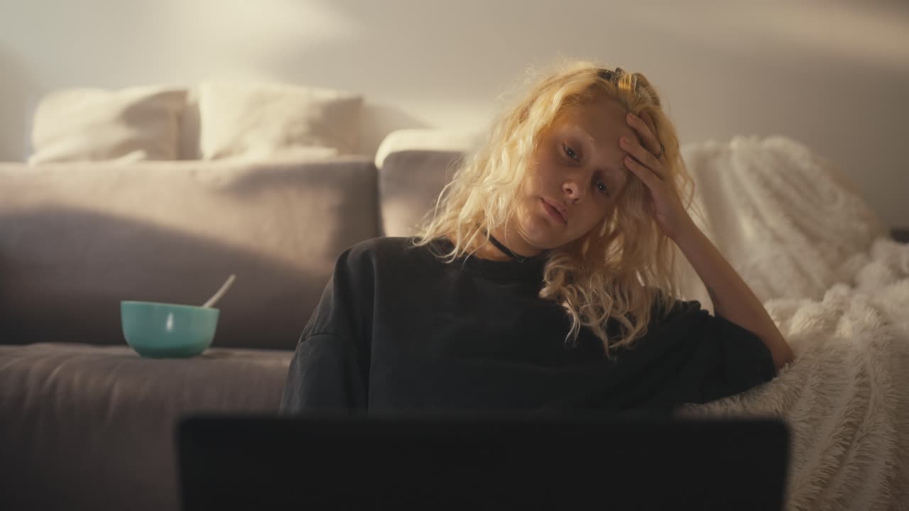 Sad tired blonde girl closes laptop and gets up near the sofa late at night