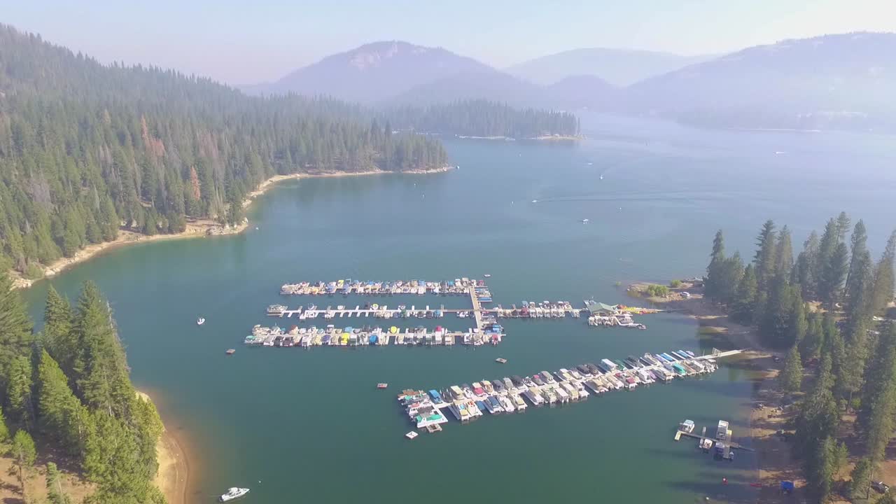 sobrevuelo aéreo de un pequeño puerto deportivo con barcos atracados en el lago shaver en las montañas de sierra nevada de california, con humo de incendios forestales en el horizonte