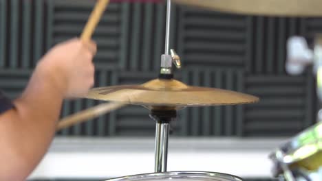 primer plano de un músico o baterista en un estudio de música sentado frente a un conjunto de tambores tocando el címbal mientras vibra al ritmo de la música