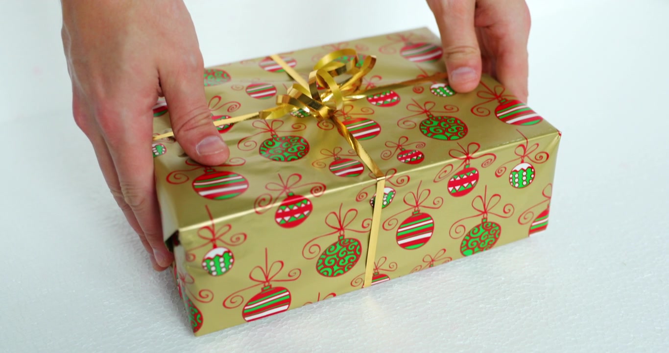 Hands lifting and laying a golden Christmas or birthday wrapped gift in gold foil and white ribbon in slow motion capture at 120fps
