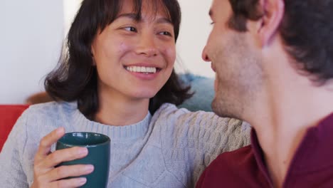 Video-of-back-view-of-happy-diverse-couple-sitting-on-sofa-and-drinking-coffee