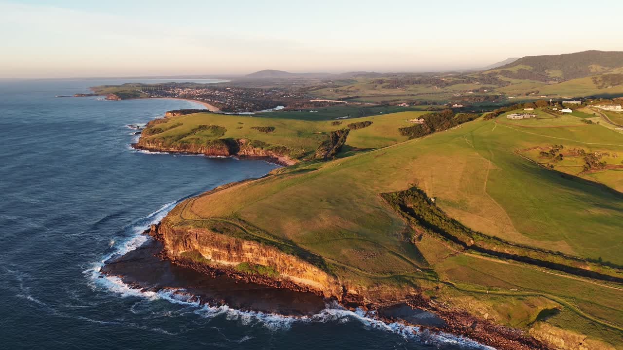 Lush green coastal farmland meets the sea in Kiama, Australia, aerial pullback perspective