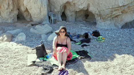 tourist woman sitting on the pebble beach of agia eleni in greece - wide, static