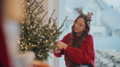 mujer decorando el árbol con luces brillantes en casa