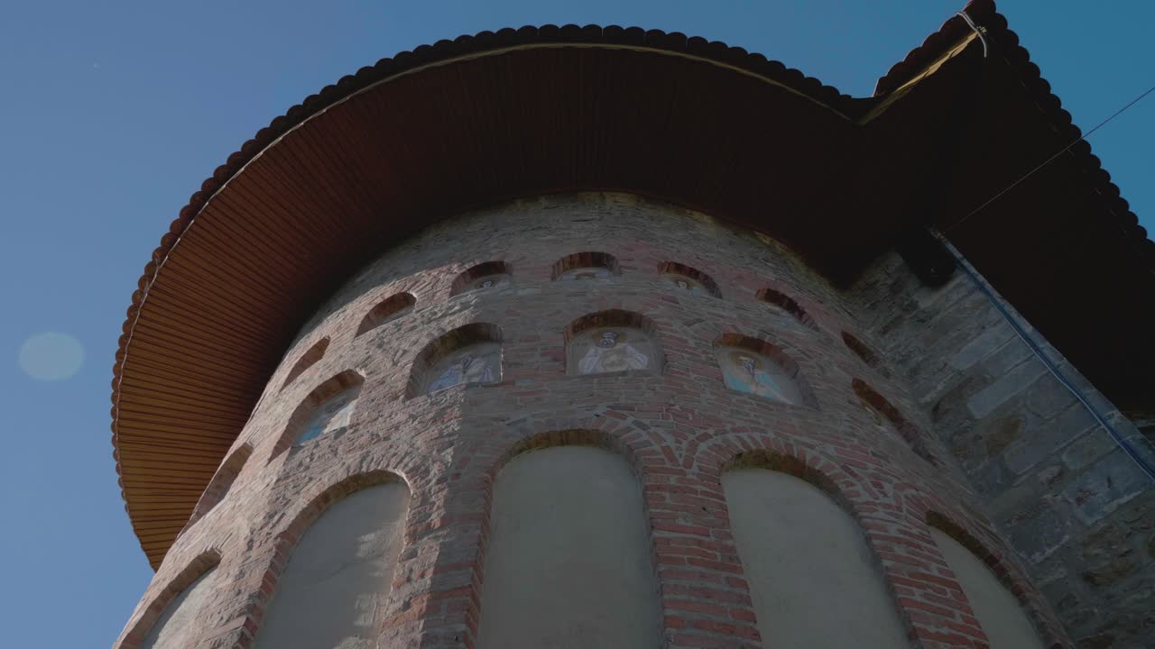 A cinematic, slow-motion close-up tilts up the tower of the historic Precista Church in Bacau, Romania, revealing medieval stone and brick architecture and small frescoes
