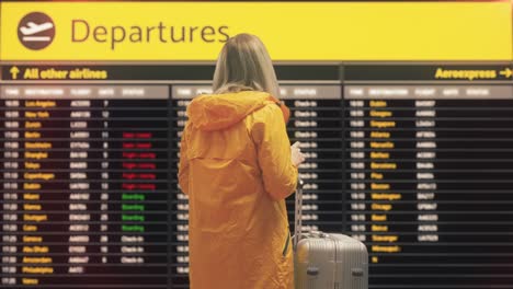 mujer viajera con maleta comprobando la información en el tablero de salida del aeropuerto