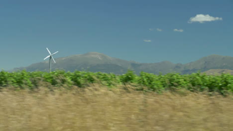 Conduciendo-Por-Un-Viñedo-Con-Un-Pequeño-Molino-De-Viento-Y-Montañas-Al-Fondo-En-Cámara-Lenta---Distrito-Vinícola-De-Marlborough,-Nueva-Zelanda